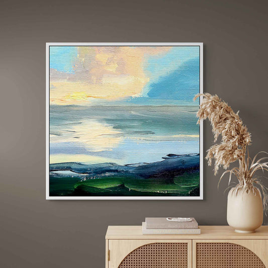 Peaceful canvas painting of dramatic clouds above the sea on a wall above a wooden cabinet with decorative items.