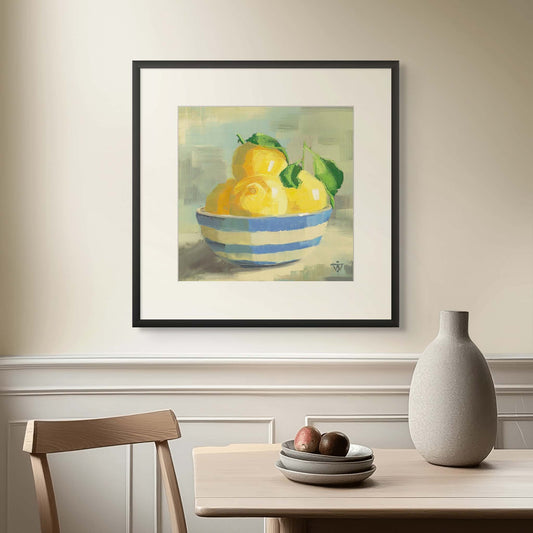 Framed painting of lemons in a striped bowl on a wall above a table with a vase and fruit.