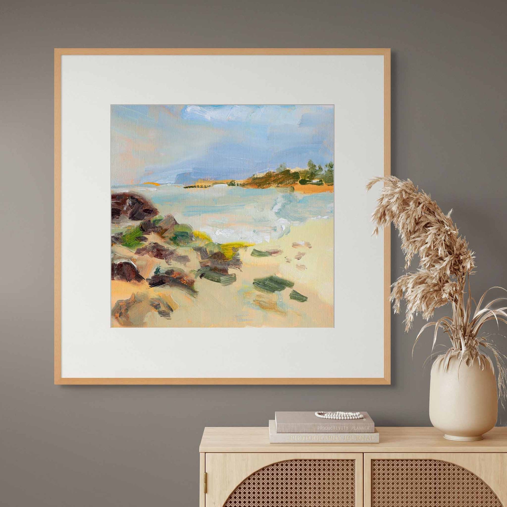 Framed painting of a coastal scene on a wall above a console table with decorative items.