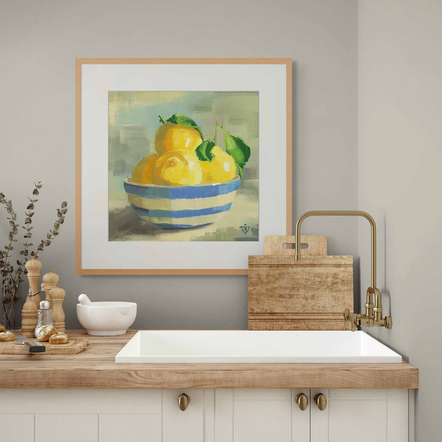 framed artwork of lemons with leaves in cornish striped bowl in modern kitchen with wooden counter, white sink and brass tap.
