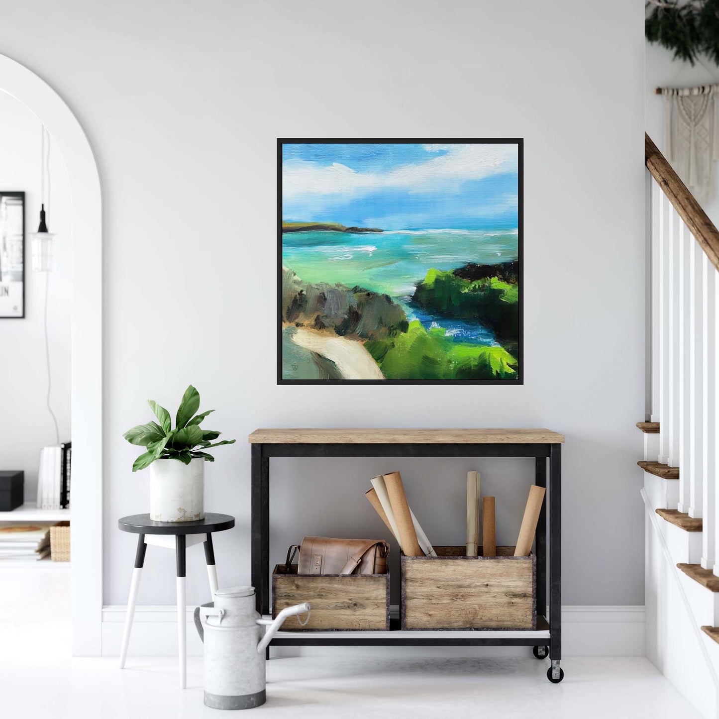 Framed painting of coastal cliffs and sea above a hallway table in a white entrance hall interior.