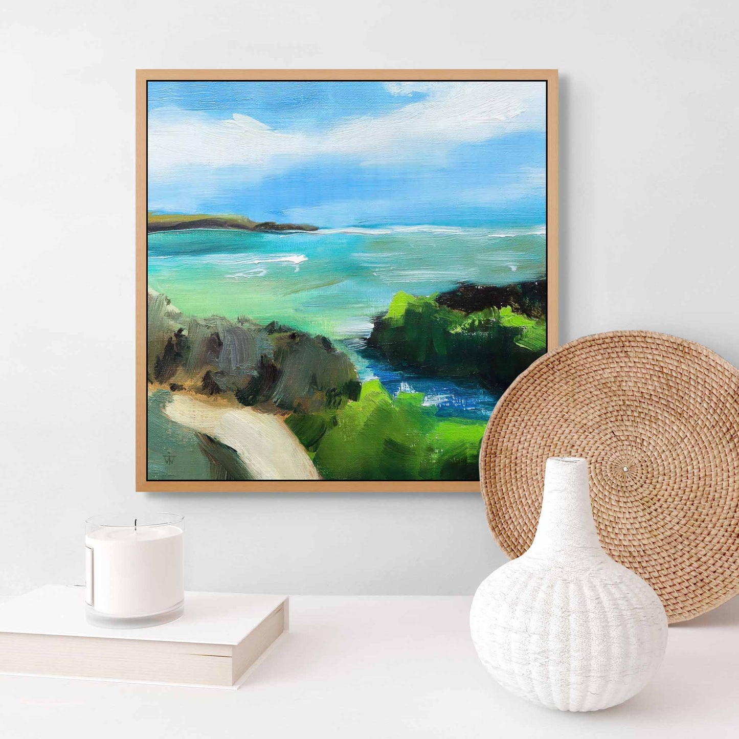 Small framed gallery wrapped canvas art of a coastal landscape on a wall with decorative items below.