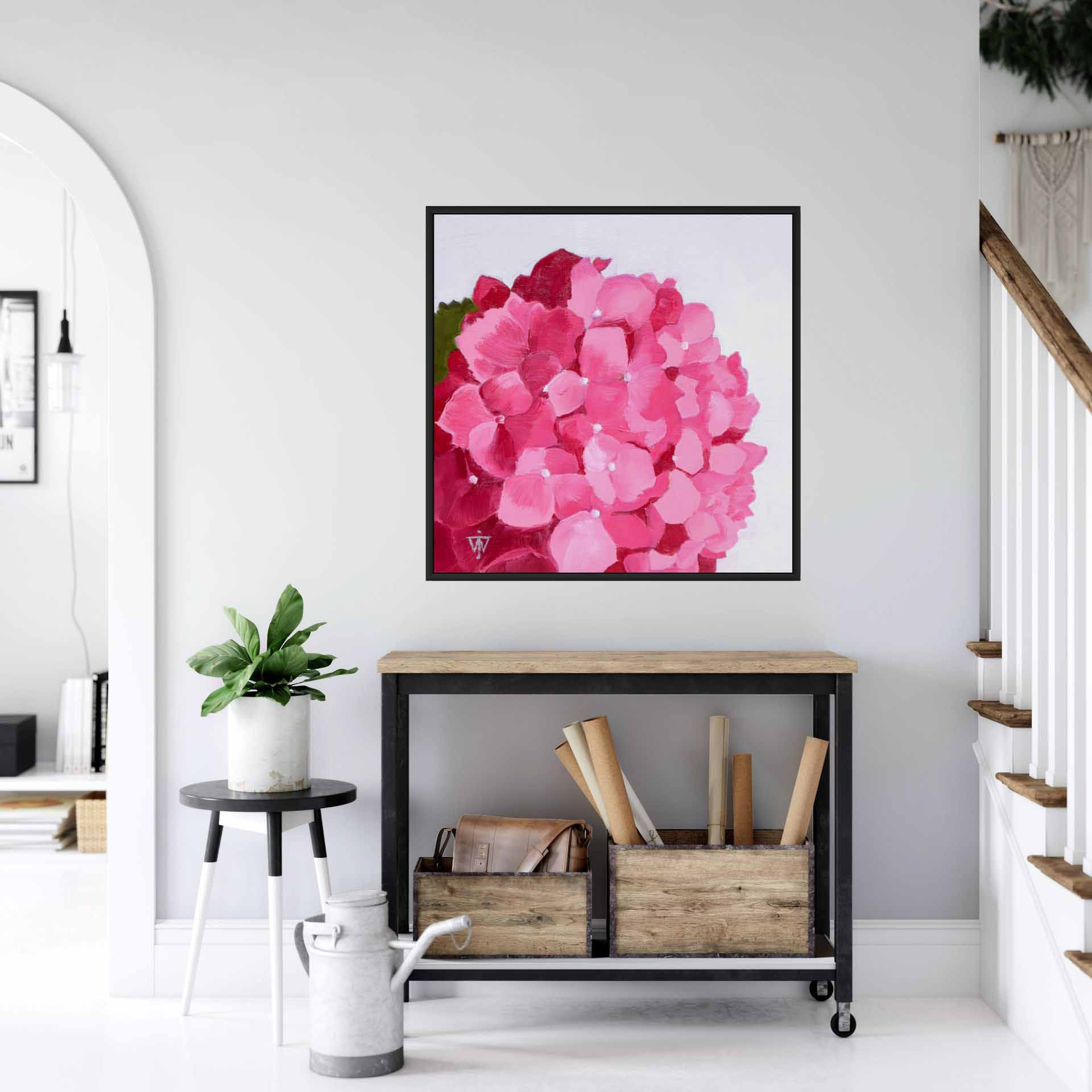 Large square framed pink floral artwork on a white wall above a small console table in a white hallway interior.