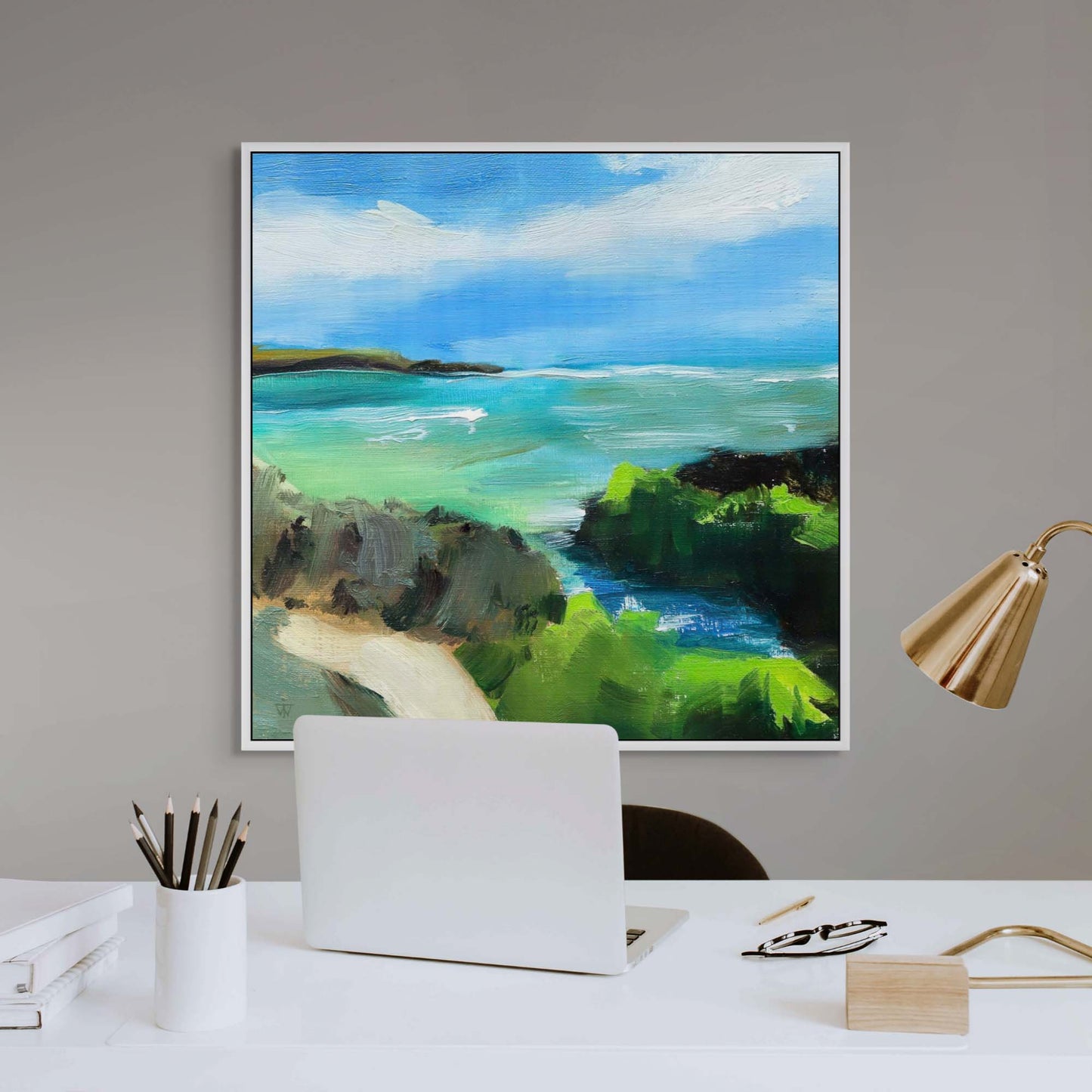 Framed art canvas print of turquoise sea and blue sky with green cliffs above a white desk.