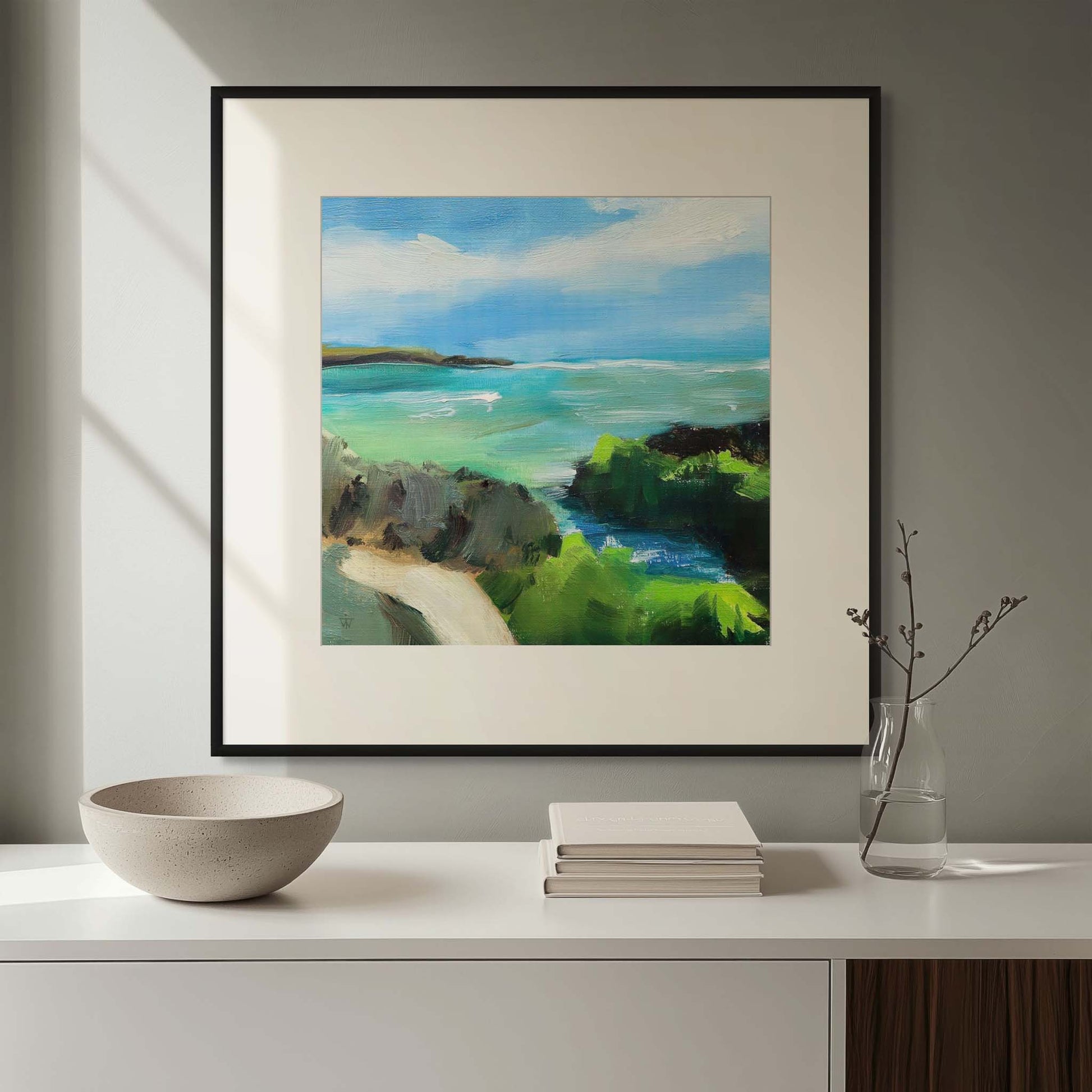 Framed painting of a coastal scene on a wall above a white sideboard in living room.