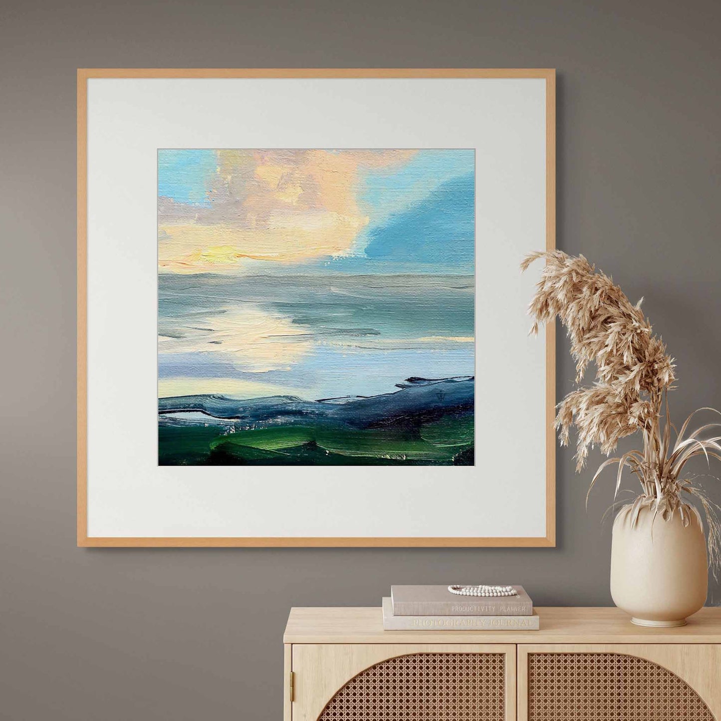 Framed print of a hand-painted oil painting on a grey wall above a wooden cabinet with decorative items.
