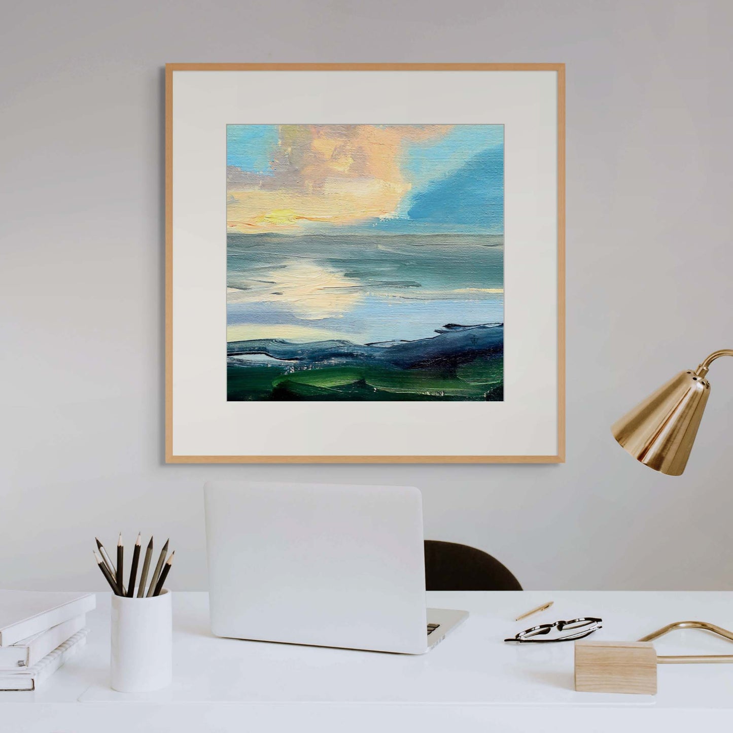 Framed artwork of a landscape with a white desk and brass lamp in a home office interior