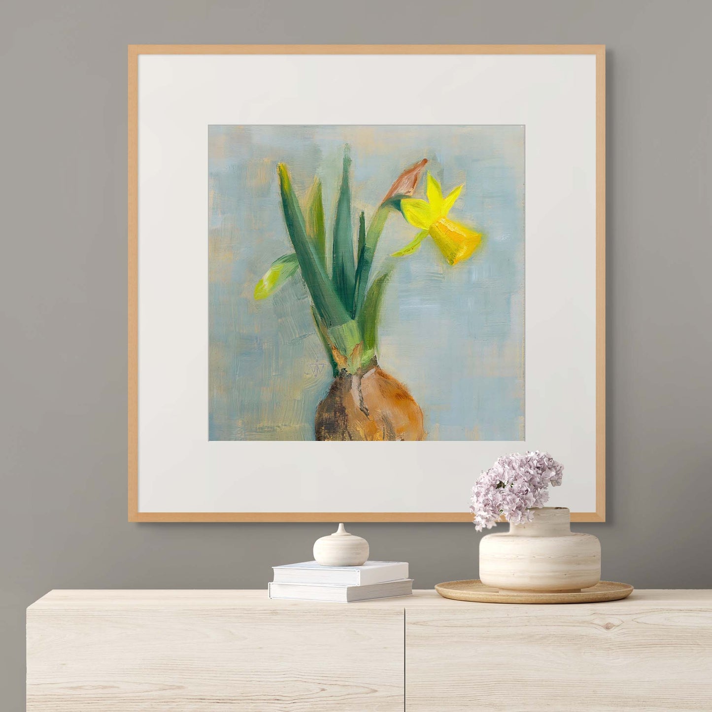 Framed painting of daffodil flowers with bulb on a wall above a wooden cabinet with decorative items.