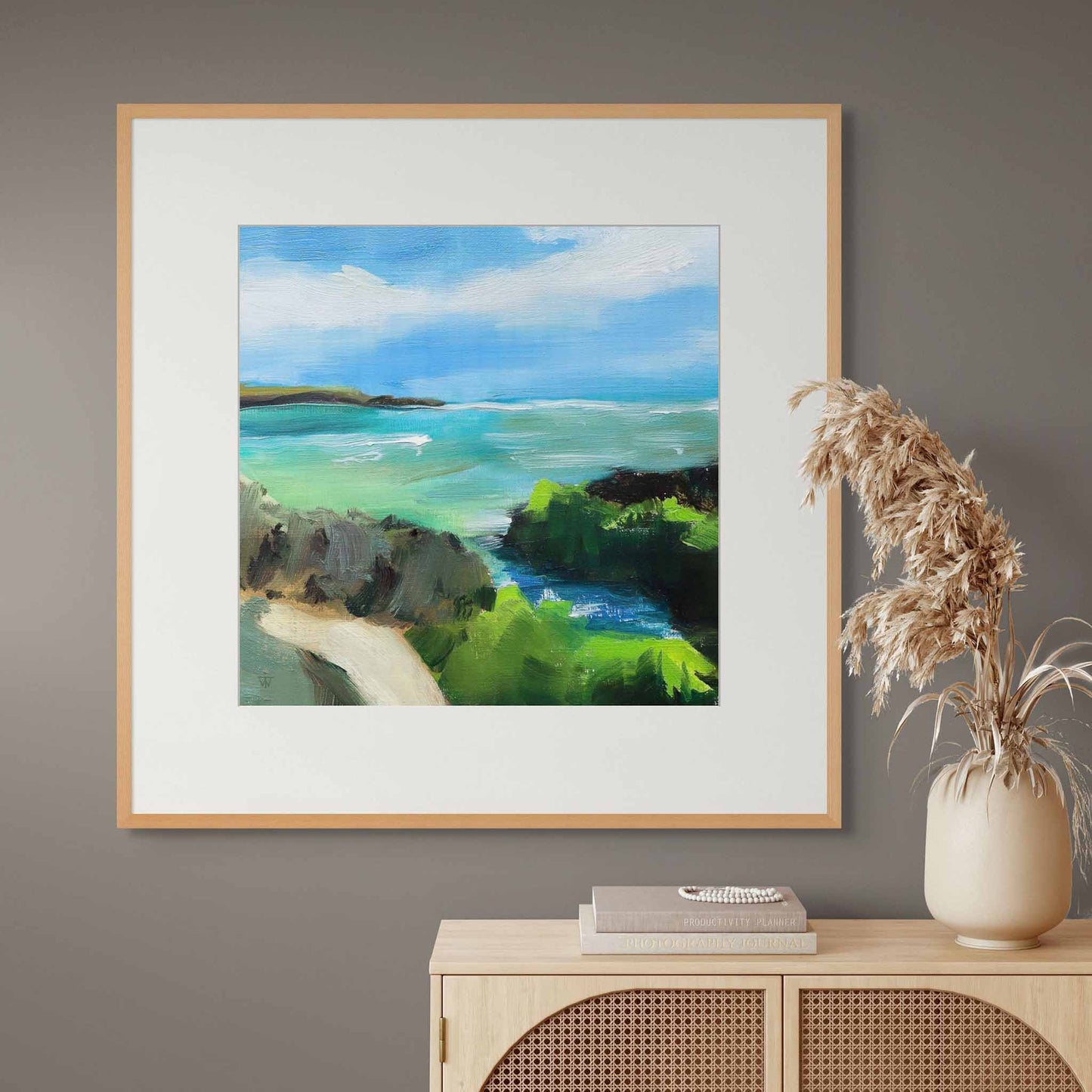 Framed painting of an abstract coastal scene on a wall above a cabinet with decorative items.