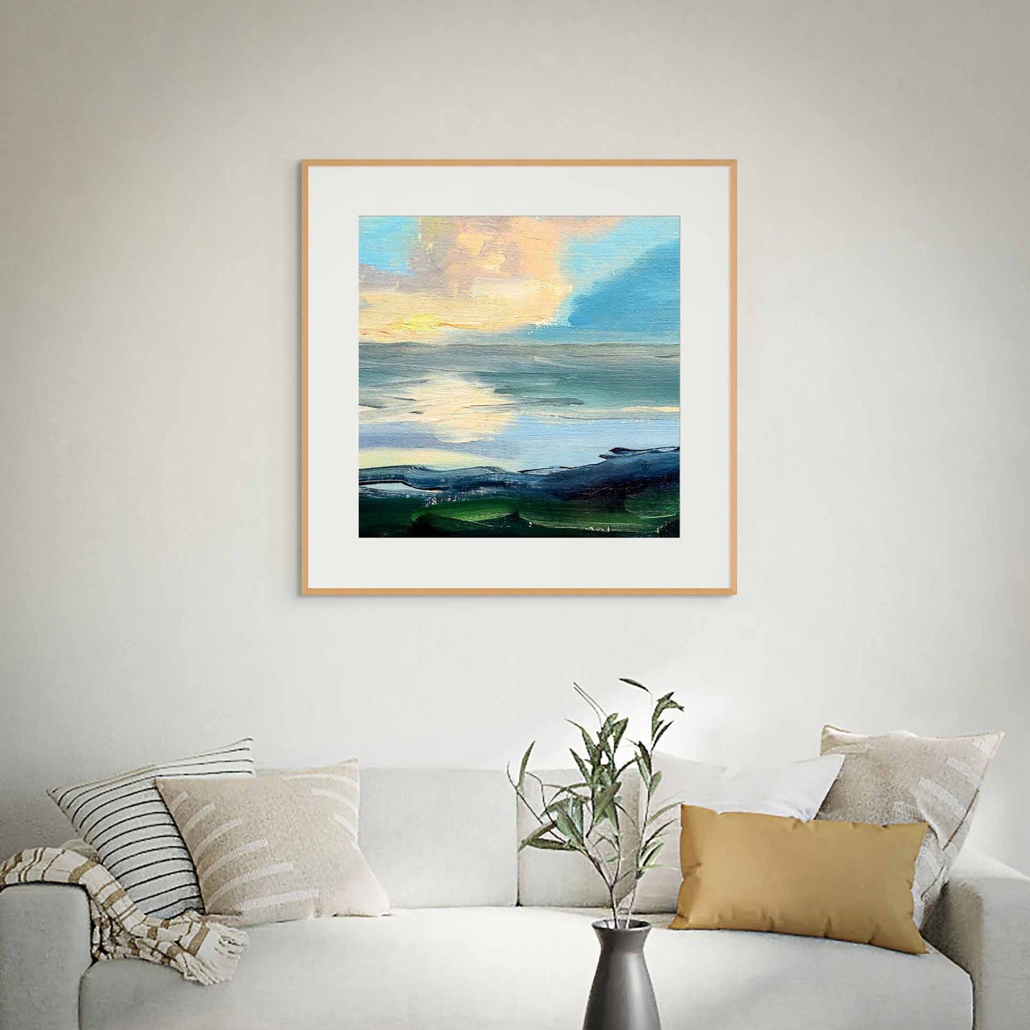 Framed artwork of a landscape with a blue sky and clouds, displayed on a wall above a sofa.
