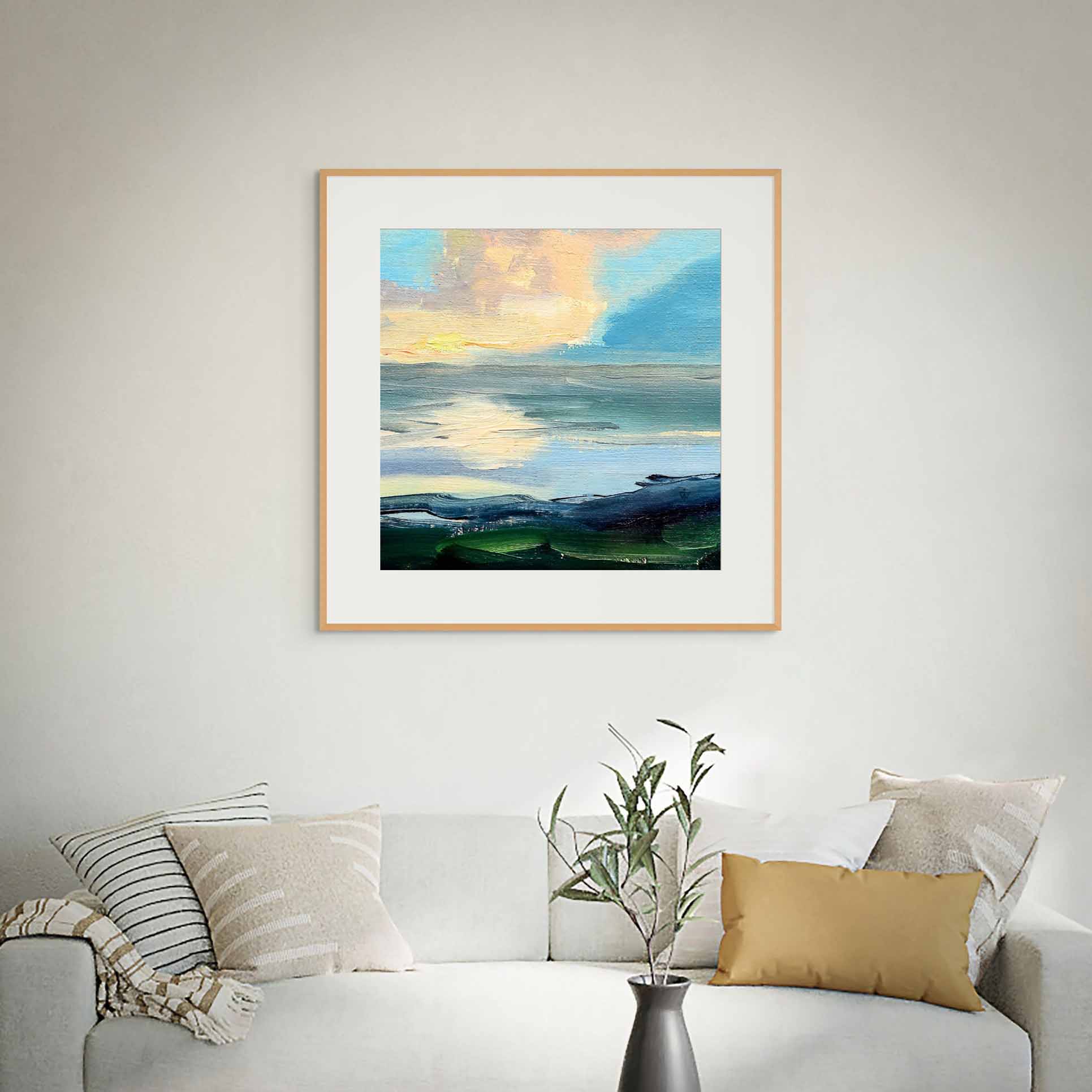 Framed artwork of a landscape with a blue sky and clouds, displayed on a wall above a sofa.