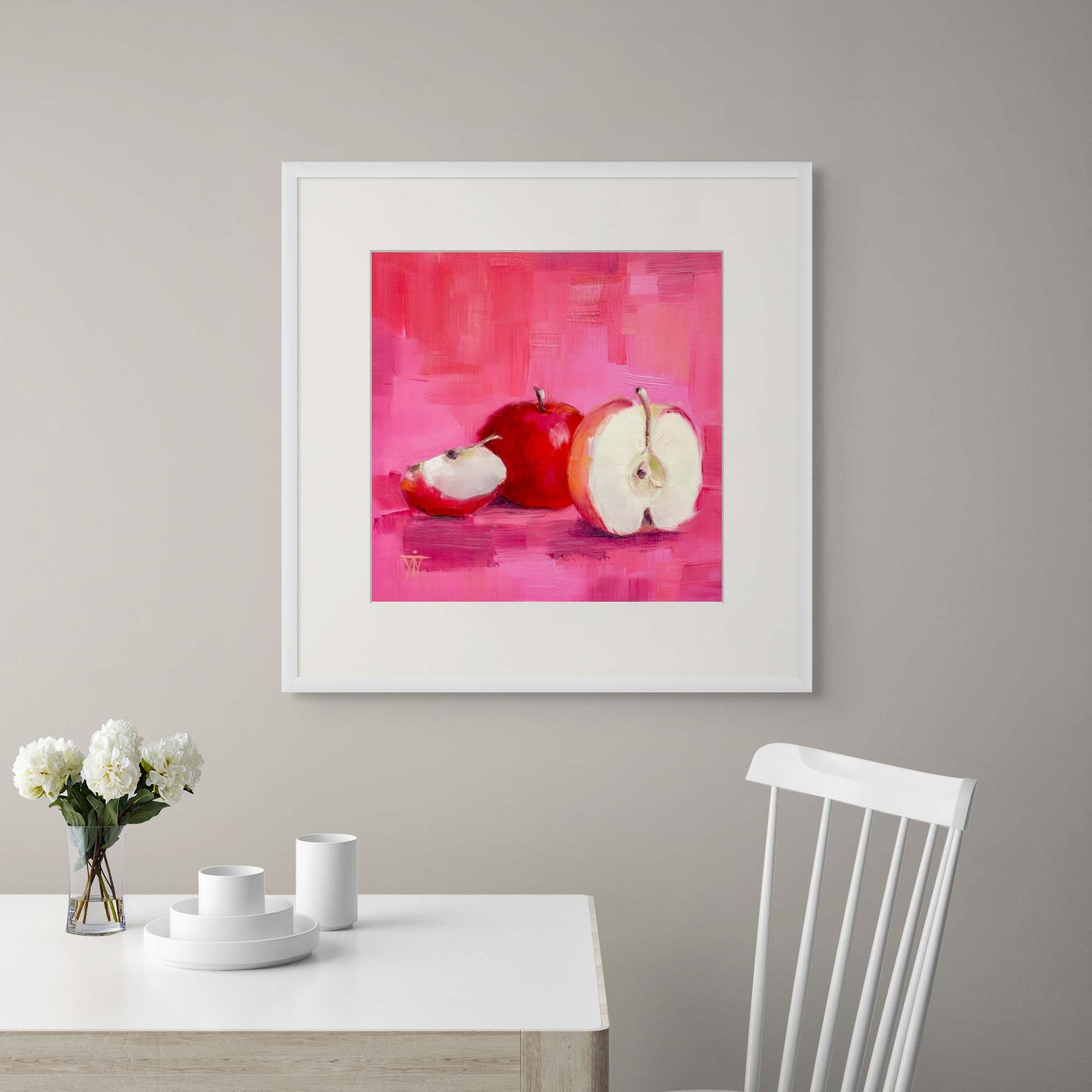 Modern artwork of apples on a pink background in white frame above a white dining table with decor items.