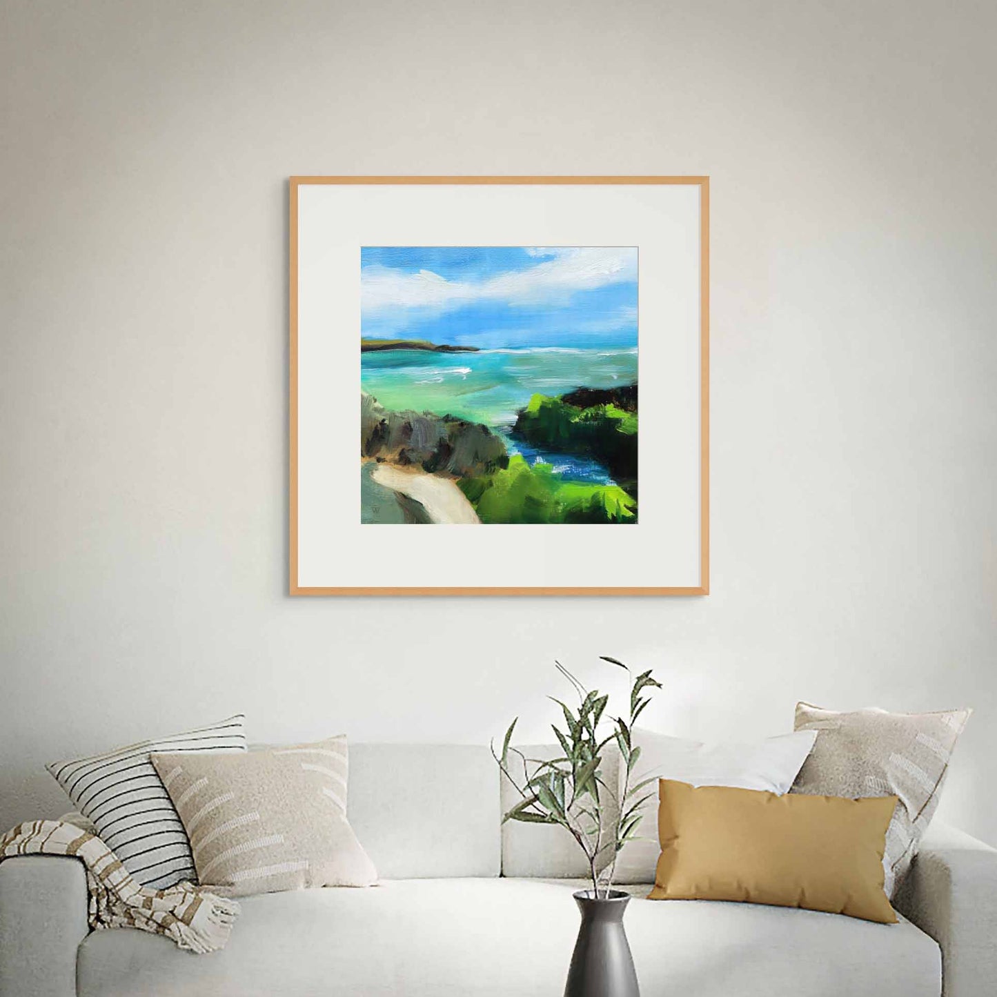 Framed painting of a coastal scene above a sofa with decorative pillows and a plant.