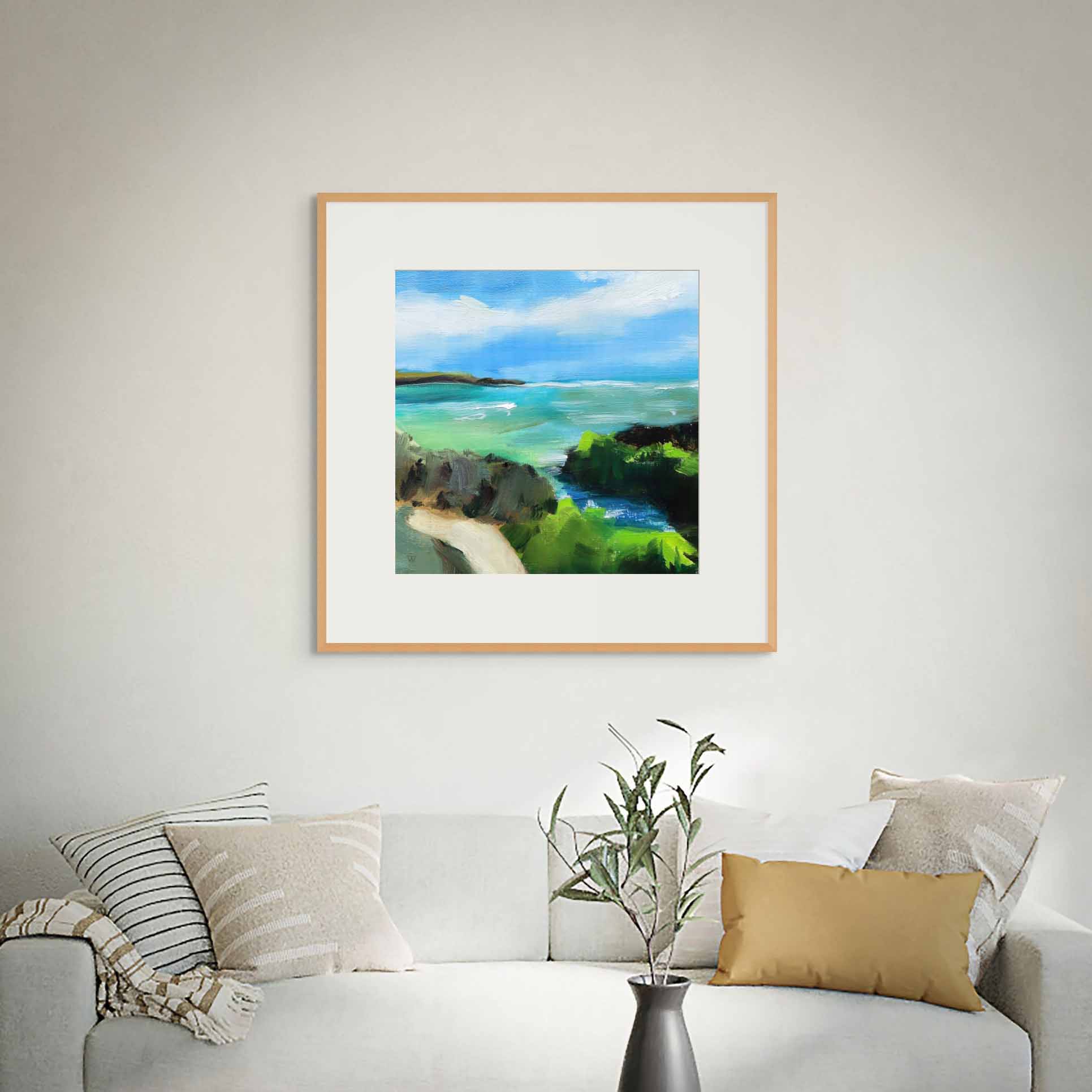 Framed painting of a coastal scene above a sofa with decorative pillows and a plant.